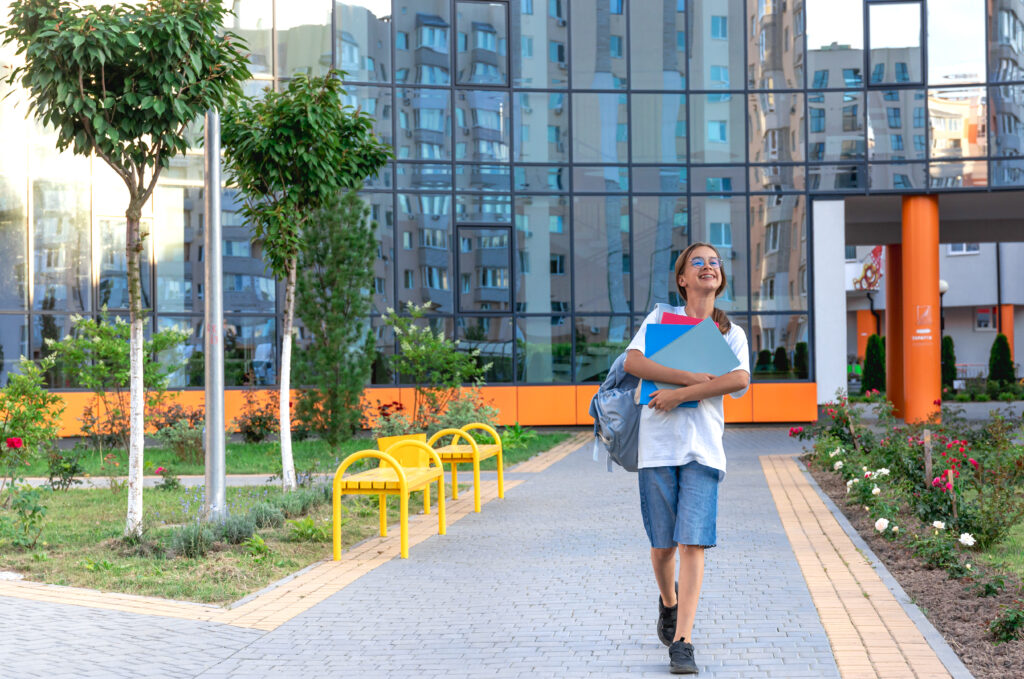 Schoolgirl with a notebook in her hands. Sunset on the background of the school. Goes to school.