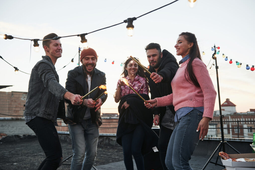 These people are happy to celebrate together. Playing with sparklers on the rooftop. Group of young beautiful friends