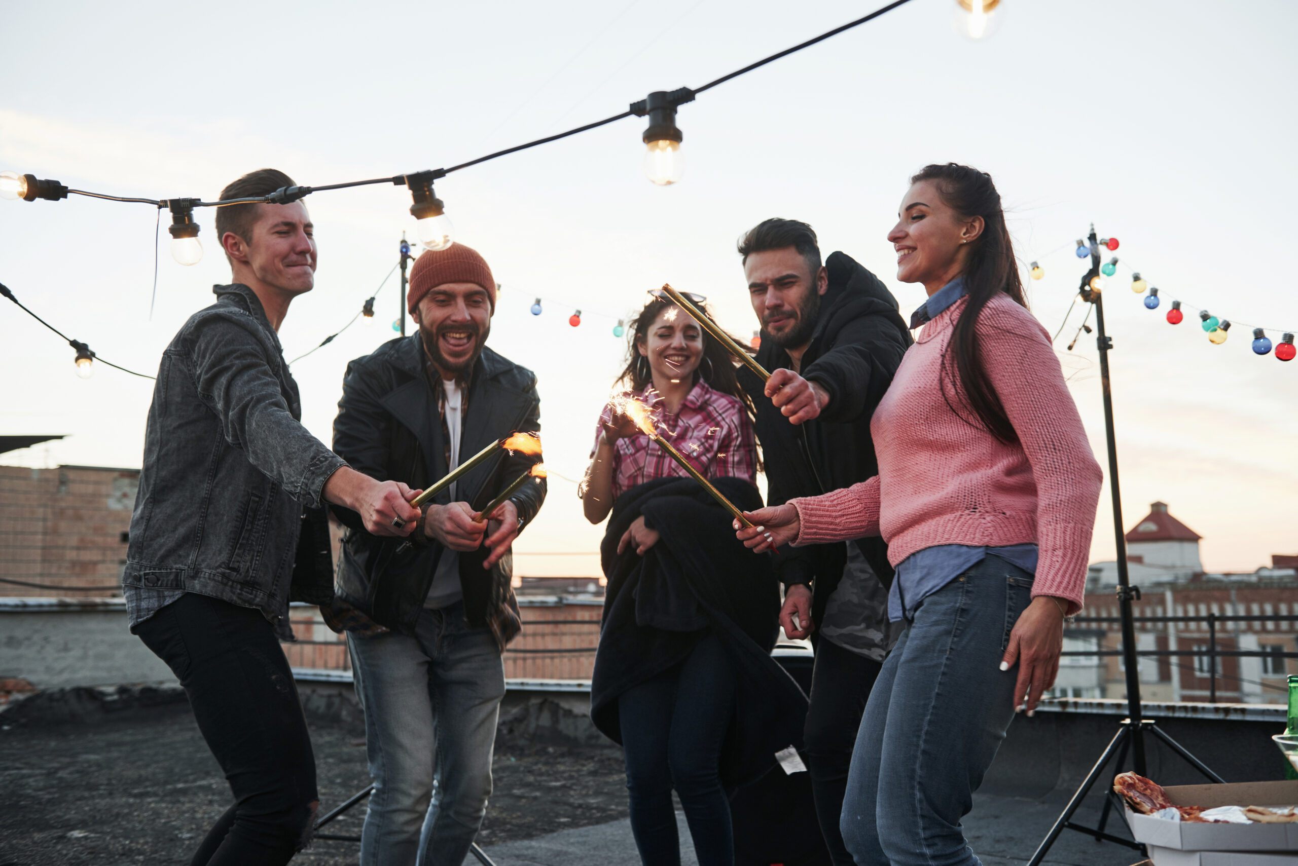 These people are happy to celebrate together. Playing with sparklers on the rooftop. Group of young beautiful friends
