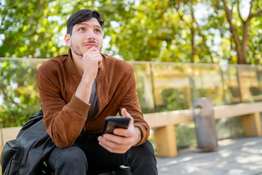 retrato de joven guapo con su telefono movil mientras esta sentado al aire libre comunicacion y concepto urbano