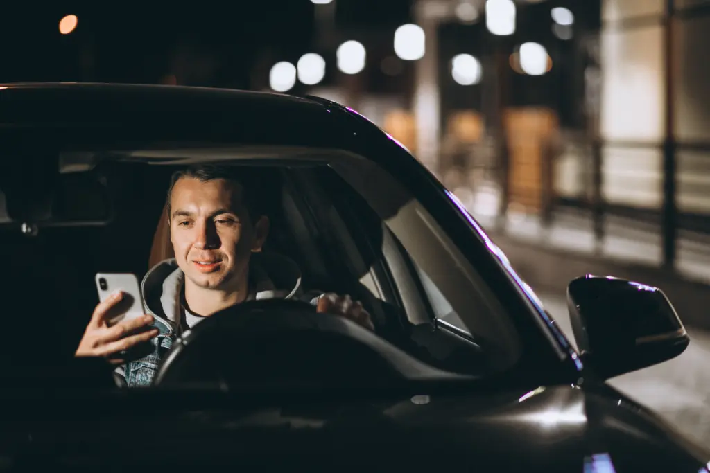 young man driving his car night time talking phone