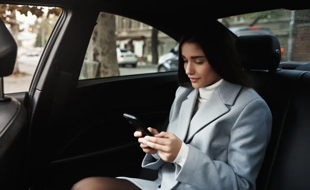 la empresaria viajando en automovil en el asiento trasero leyendo un mensaje de texto en el telefono inteligente mientras conduce en la reunion