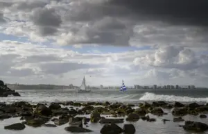 paisaje de la orilla rodeada por el mar con barcos y surfistas bajo un cielo nublado