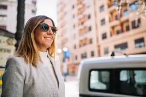 mujer joven elegante sonriente con las gafas de sol en la calle cerca del coche