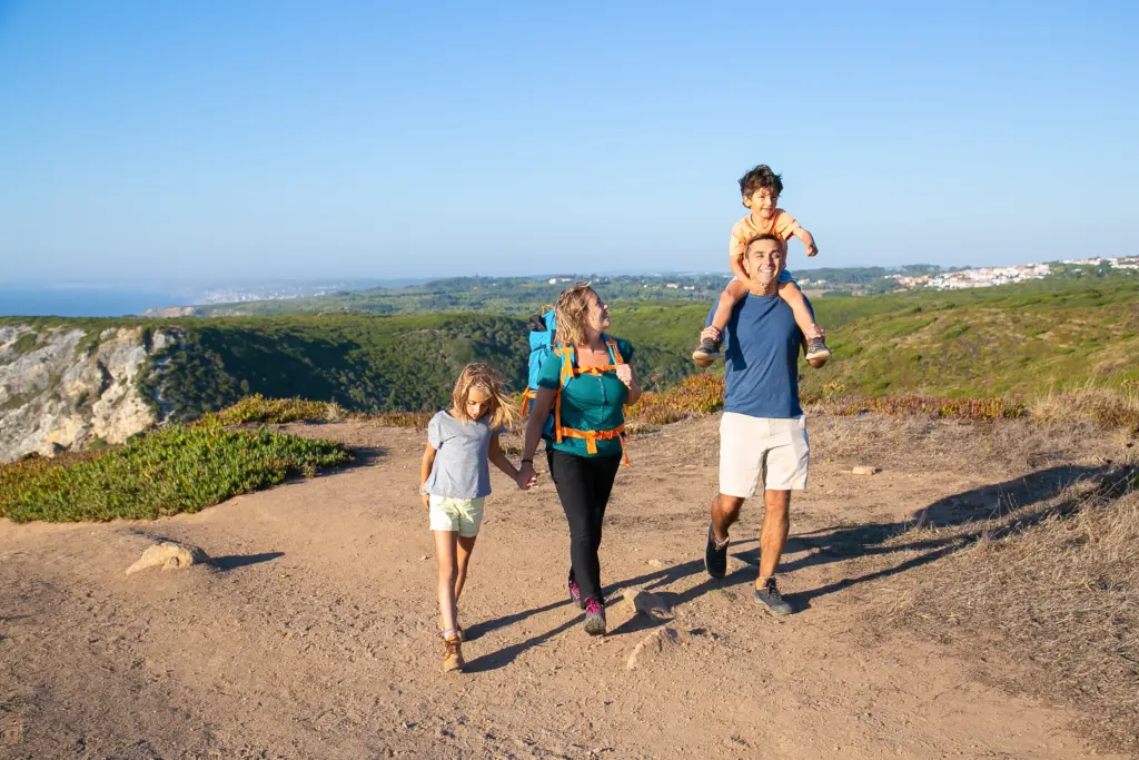 familia feliz pareja y ninos senderismo en el campo caminando por el sendero muchacho emocionado montando en el cuello de los papas longitud total concepto de naturaleza y recreacion