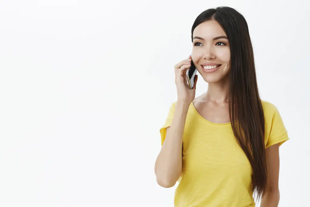 encantadora chica sin maquillaje sosteniendo el smartphone cerca de la oreja medio girada mirando la izquierda con una amplia sonrisa despreocupada t