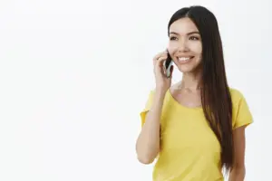 encantadora chica sin maquillaje sosteniendo el smartphone cerca de la oreja medio girada mirando la izquierda con una amplia sonrisa despreocupada t