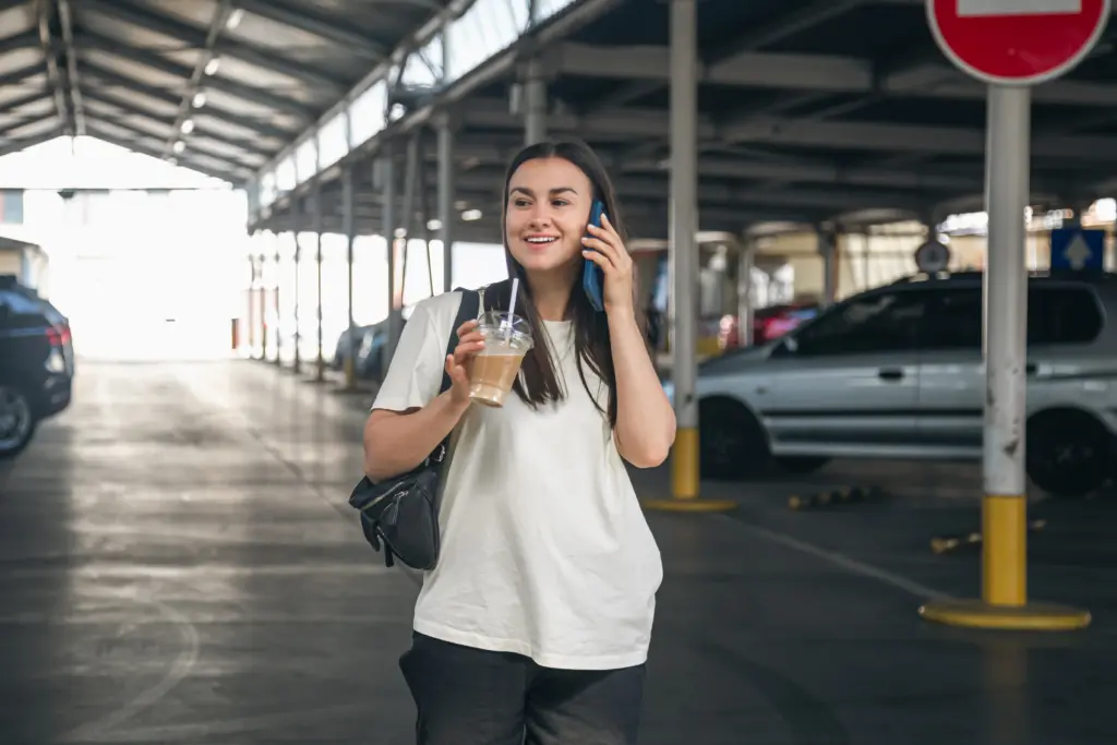 young woman with coffee talking phone parking lot