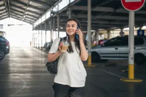 young woman with coffee talking phone parking lot