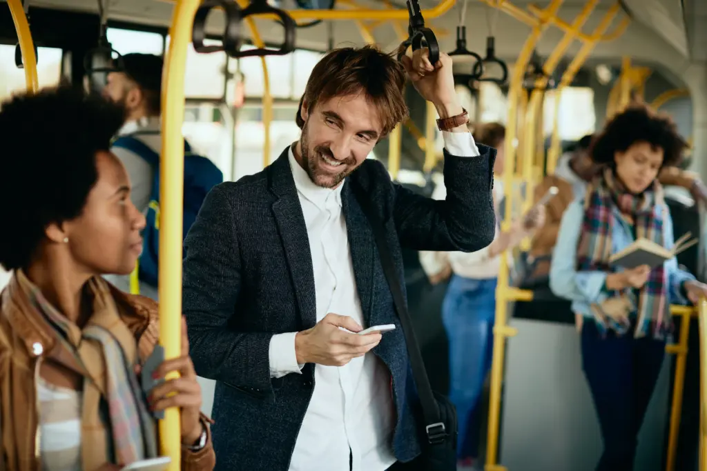 hombre feliz usando telefono celular y hablando con un pasajero mientras viaja en autobus