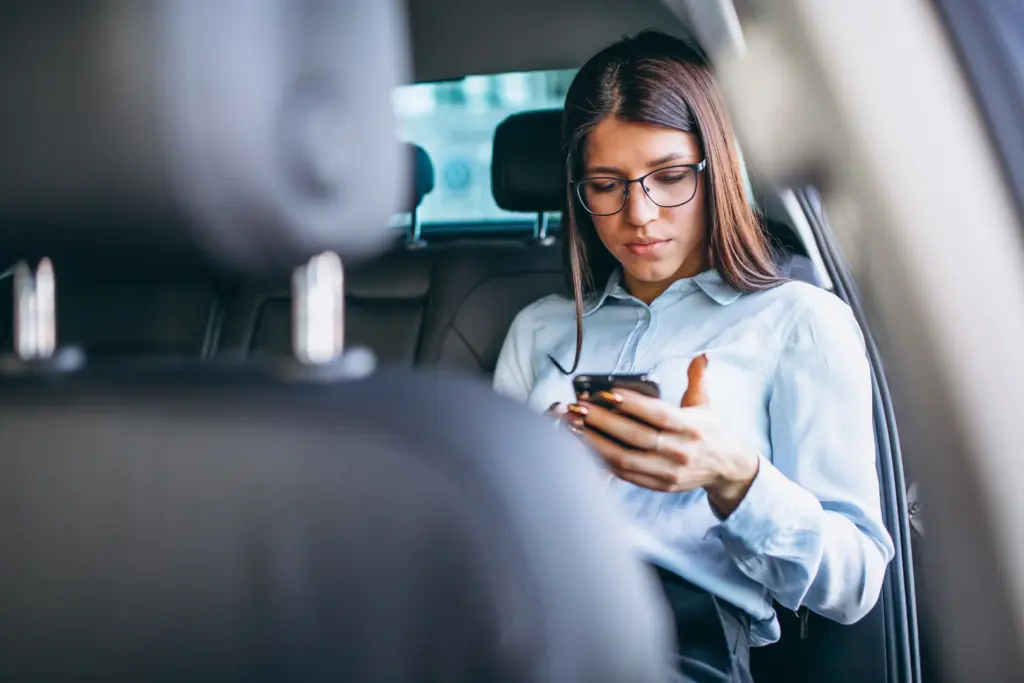 mujer de negocios que se sienta en coche y que usa el telefono