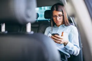 mujer de negocios que se sienta en coche y que usa el telefono