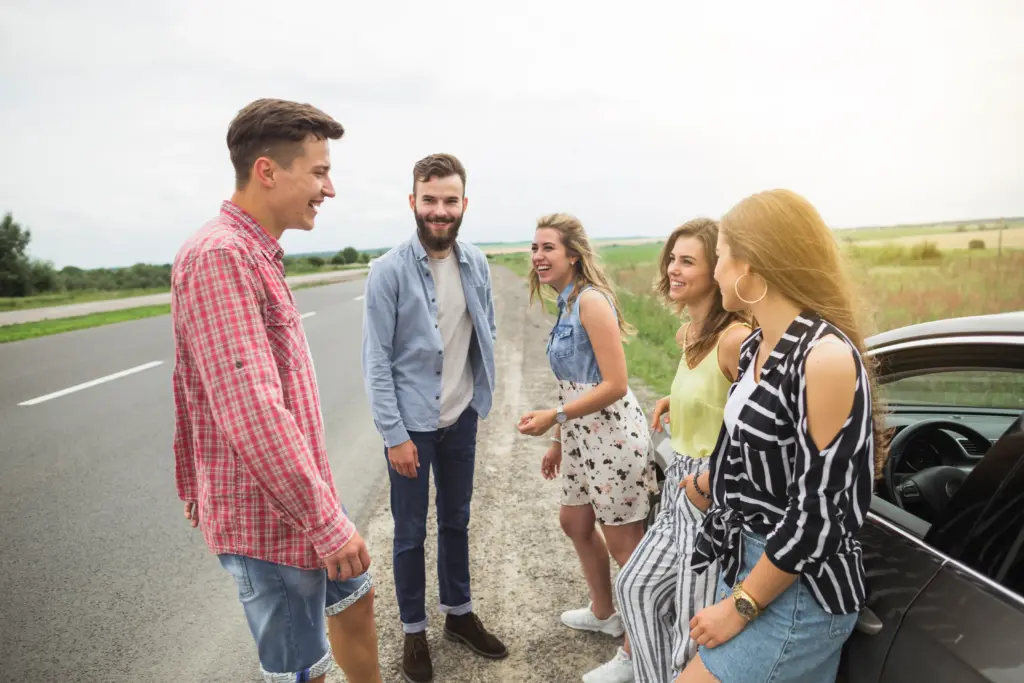 happy friends standing outside car enjoying road