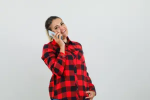 senora joven hablando por telefono movil en camisa cuadros y mirando alegre