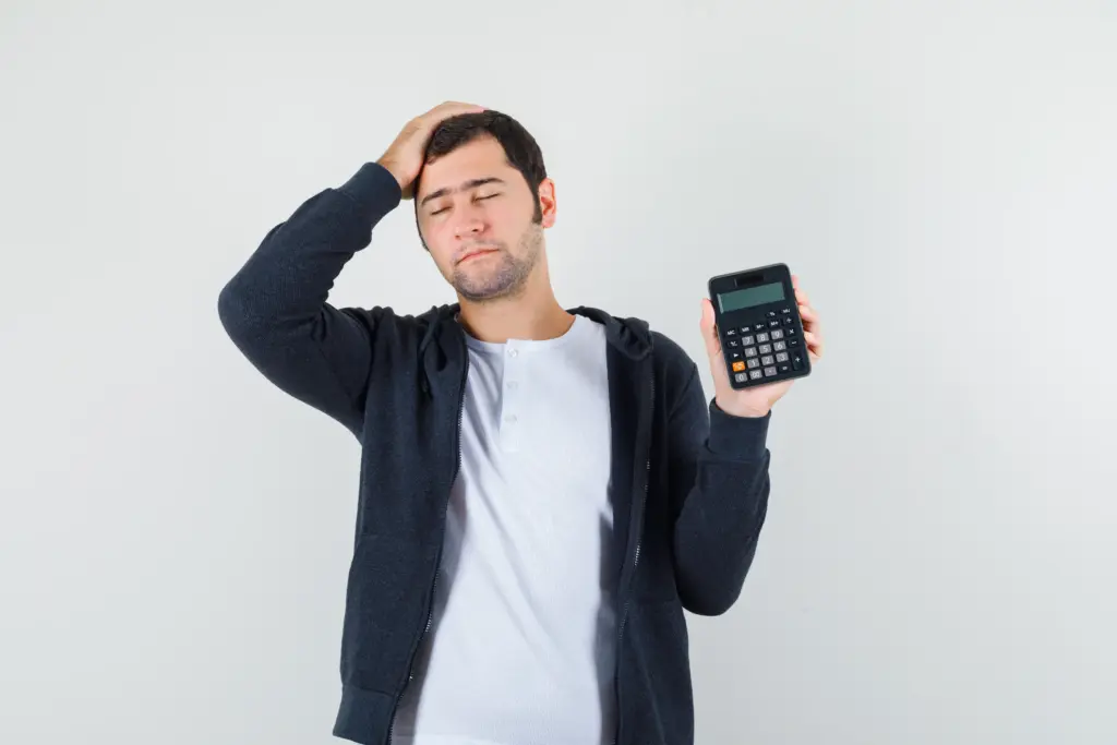 hombre joven con camiseta blanca y sudadera con capucha negra con cremallera frontal que sostiene la calculadora y pone la mano en la cabeza y se ve optimista vista frontal