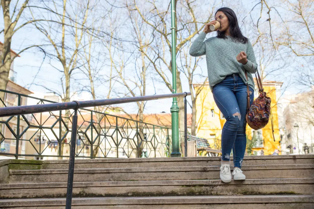 young woman walking down city stairs drinking coffee